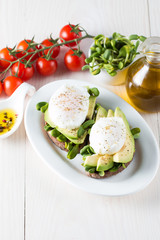 Avocado toast, cherry tomato on wooden background. Breakfast with toast avocado, vegetarian food, healthy diet concept. Healthy sandwich with avocado and poached eggs.