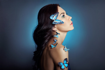 Beautiful mysterious woman with butterflies blue color on her face, brunette and paper artificial...