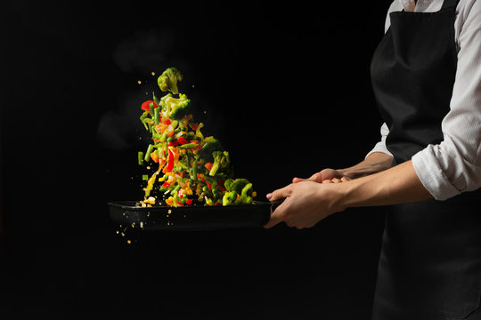 Flying mixed vegetables in a pan. Diet healthy food. Black background for copying text. Concept of food and cooking.