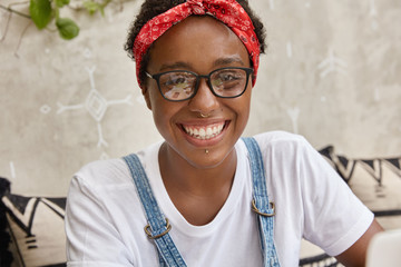 Close up of happy woman with joyful expression, pleased look, rejoices positive moments in life, has funny face, wears awkward spectacles and headband, dressed in casual t shirt. Ethnicity concept