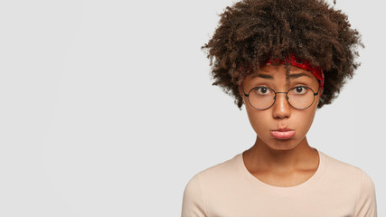 Indoor shot of dejected woman with dissatisfied expression, purses lower lip, feels lonely, has...