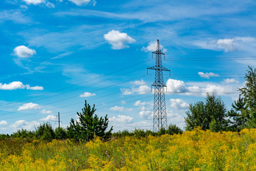 High-voltage power line in a field against a blue sky with clouds