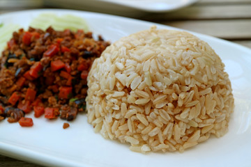 Closed Up Steamed Thai Brown Jasmine Rice with Blurred Sauteed Vegetables Served on White Plate