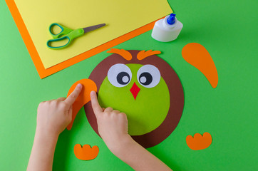 kid is making a owl with color paper, glue and scissors, on green