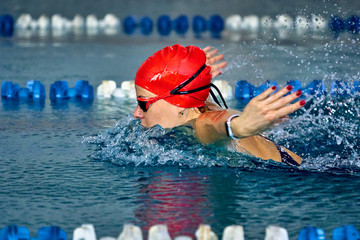 Female athlete swims with a butterfly style. Splashes of water scatter in different directions.