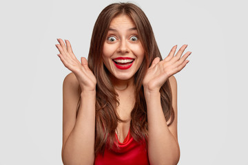 Headshot of woman with cheerful expression keeps palms near face, reacts on positive news, cant...