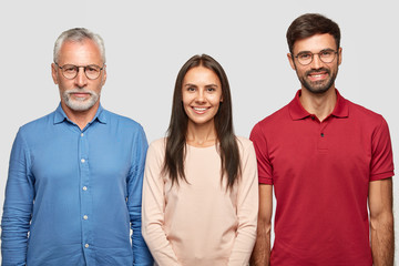 Three people in shot. Serious senior male pensioner dressed in formal shirt, stands near his daughter and son, pose together against white backgrounf for making family portrait. Relationships concept