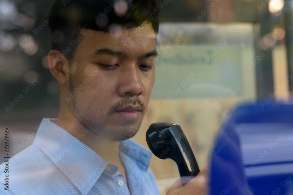 Sticker Young Asian businessman using the payphone outdoors