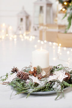 Christmas candles and snowy fir branches over white wooden background with lights.  New Year's decoration with a fir tree in white tones.