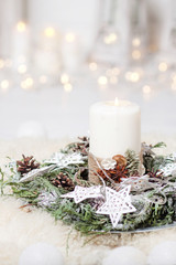 Christmas candles and snowy fir branches over white wooden background with lights.  New Year's decoration with a fir tree in white tones.