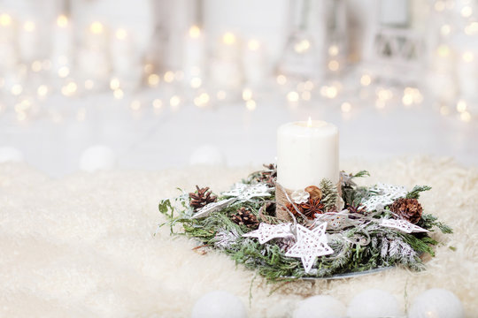 Christmas candles and snowy fir branches over white wooden background with lights.  New Year's decoration with a fir tree in white tones.