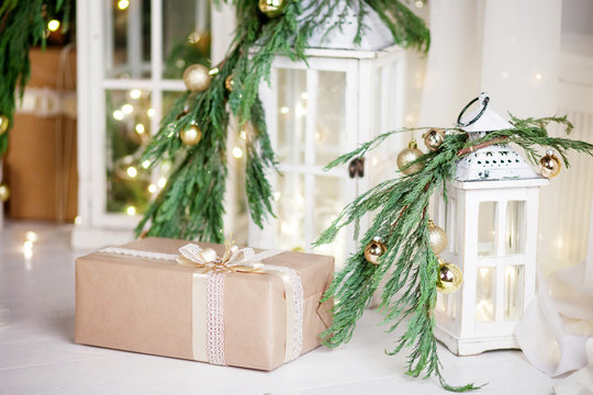 Christmas box and lantern over white wooden background with lights.  New Year's decoration with  fir branches in white tones.