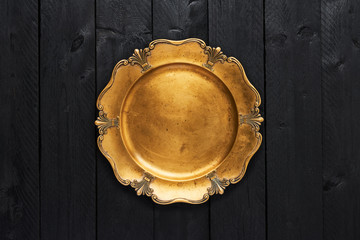 Top view of old golden serving plate on black wooden table with copy space.