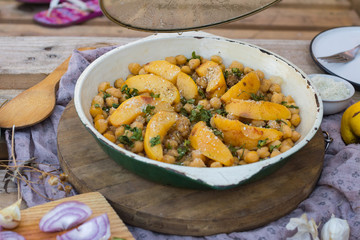 Woman hands open lid of baked chickpea with quince in cast iron skillet, frying pan. Vegan vegetarian lunch, paleo diet, healthy dinner served with salad and vegetables on table