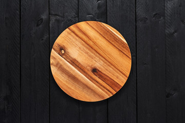 Top view of round wooden serving plate on black wooden table with copy space.