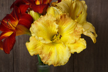 A bouquet of flowers of red and yellow daylily flower on the background of a textural old board.