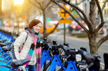 Fototapeta na wymiar Happy young woman tourist ready to ride a rental bicycle in New York City at sunny spring day. Female traveler enjoying her time in downtown Manhattan.