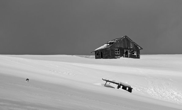 Black and white picture of an abandoned shepherd cottage in the mountains during winter with snow