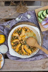 Baked chickpea with quince in cast iron skillet, frying pan with wooden spatula on it. Vegan vegetarian lunch, paleo diet, healthy dinner served with salad and vegetables on table. Top view