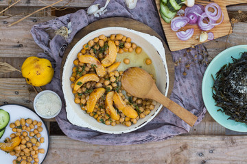 Baked chickpea with quince in cast iron skillet, frying pan with wooden spatula on it. Vegan vegetarian lunch, paleo diet, healthy dinner served with salad and vegetables on table. Top view