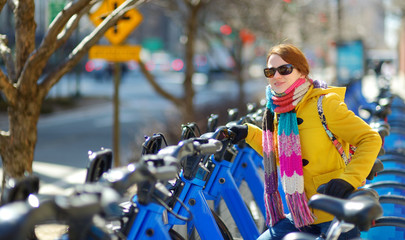 Happy young woman tourist ready to ride a rental bicycle in New York City at sunny spring day. Female traveler enjoying her time in downtown Manhattan.