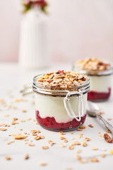 Healthy breakfast. Two jars of healthy yogurt with strawberry sauce and oat on white marble table....