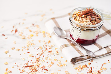 Healthy breakfast. Jar of healthy yogurt with strawberry sauce, oat and chocolate on white marble table. Close up with copy space.