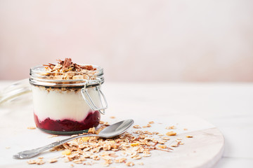 Healthy breakfast. Jar of healthy yogurt with strawberry sauce, oat and chocolate on white marble serving plate over pink background with copy space.