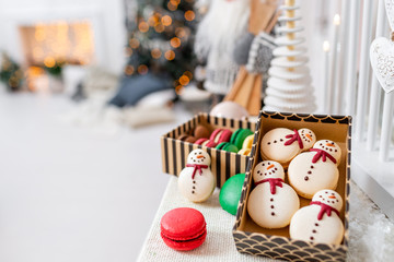 Variety of sweet macaroons in carton box. Cookie in the form of a snowman. Merry Christmas card. New year mood. lights of garland bulbs