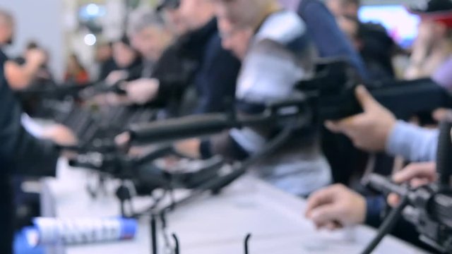 Abstract Defocused Blurred Background. Weapon optics sight of sniper rifle with man close-up. Several large-caliber weapons on table. Firearms gun submachine sniper rifle weapons close-up.
