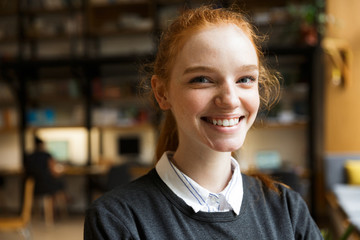 Happy redhead lady student posing indoors in library.