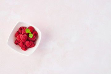 Top view of fresh sweet raspberries with mint leaves in white bowl on rose background with copy space.