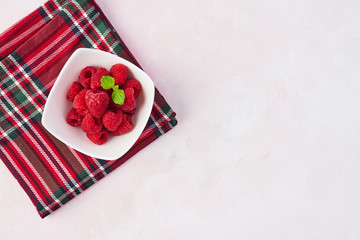 Top view of fresh sweet raspberries with mint leaves in white bowl on rose background with copy space.