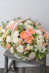 Wicker basket with mix beautiful flowers on wooden table near gray wall. Beautiful garden flowers in the arrangement , the work of a professional florist. European floral shop