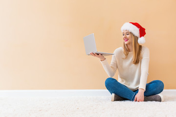 Young woman with santa hat using her laptop on a white carpet