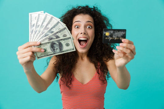 Image of delighted woman 20s wearing casual clothing holding fan of dollar money and credit card, standing isolated over blue background