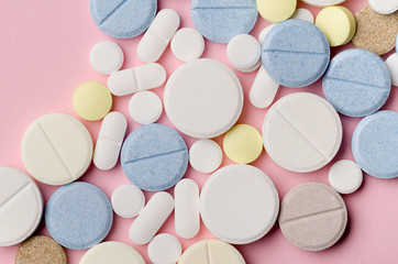 multi-colored tablets of different shapes close-up on a pink background, top view