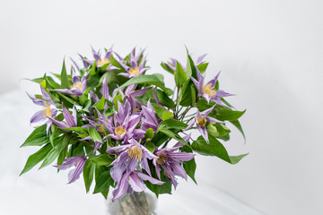 bouquet of lilac clematis flowers in glass vase. the work of the florist at a flower shop. A glass vase with flowers placed on wooden gray table