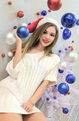 Beautiful sexy girl in knitted sweater and fur slippers is smiling. Theme of the New Year. Blue and red Christmas balls on a white background. Vertical picture.