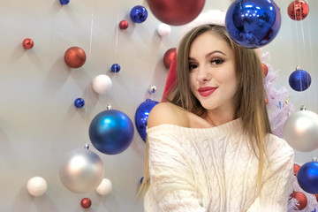 Theme of the New Year. Sweet long-haired girl looks sexy in frame. Blue and red Christmas balls on a white background.
