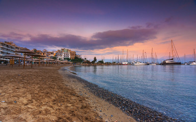 Marina with anchored fishing boats, sandy beach and the beautiful town of Agios Nikolaos at the background, Crete, Greece.