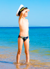 Funny child in black swimming trunks in a sea cap looking into the distance on the background of blue sea and sky
