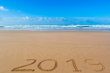2019 inscription written in the wet yellow beach sand