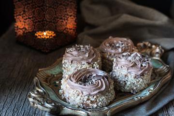 Biscuit cakes, sprinkled with nut chips and decorated with chocolate cream, are next to the candlestick with a dying candle in the background and illuminated by the morning  light from the window
