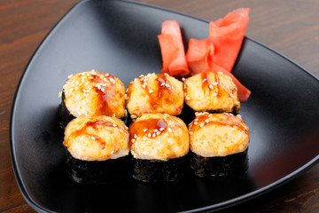 Appetizing baked hot sushi rolls. Set sushi on a black plate with ginger closeup.