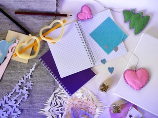 Decorative composition of festive decor, white canvas, paper, pencils, notebook, felt and paper hearts, luminous glasses, light background, top view, Christmas, Valentines, romantic greeting, seasonal
