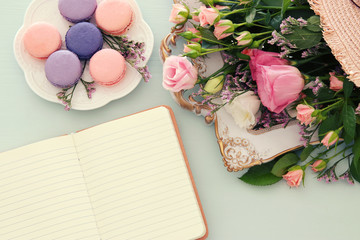 plate of macaroons over wooden table, emprty notebook and flowers.
