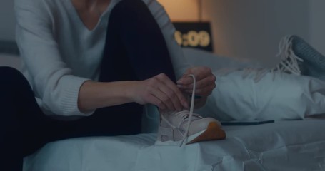 Attractive sporty young Caucasian woman getting ready for exercising early in the morning, tying her sports shoe. 4K UHD