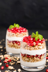 Pomegranate parfait - sweet organic layered dessert with granola flakes, yogurt and fruit seeds on black background.