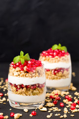 Pomegranate parfait - sweet organic layered dessert with granola flakes, yogurt and fruit seeds on black background.